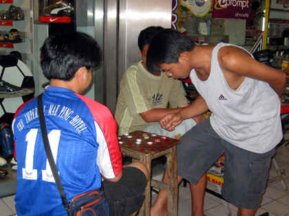 BOYS PLAYING CHECKERS WITH BOTTLE CAPS AS MARKERS