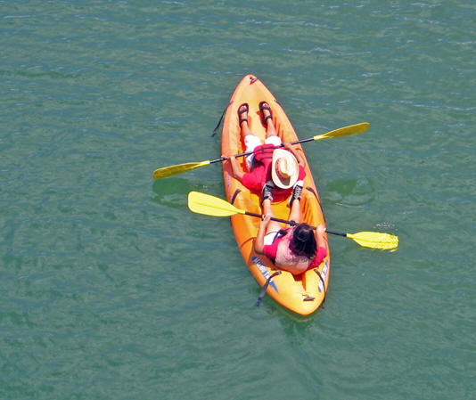 Two people paddling across the Colorado River, in a floatie boat enjoying the weather