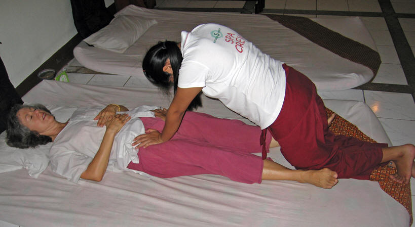 A uses the weight of her body to press down on the two main arteries from Akaisha's pelvis to her legs. Chiang Mai, Thailand